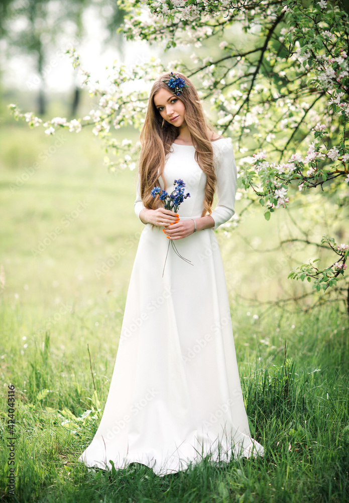 Beautiful young woman in white wedding dress with flowers enjoying a summer day in nature