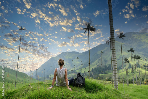  Girl with backpack sitting on green grass watching gigantic palm trees in Cocora Valley in Colombia photo