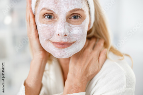 Close up of senior blond woman with nutrition mask on her face, visiting cosmetologists in modern medical center