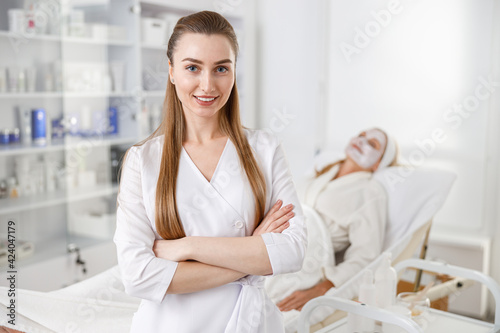 Dermatologist with hands crossed standing by a patient lying on the couch while medical procedure.