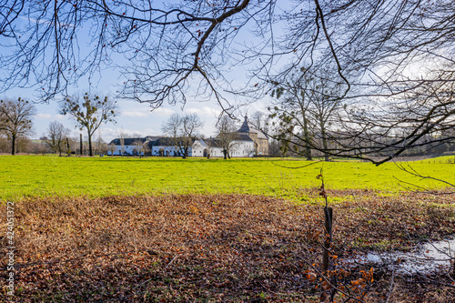 Dutch meadow with brown and green grass, bare trees with Genhoes castle in the background, sunny day with a blue sky in Valkenburg aan de Geul in South of Limburg, Netherlands photo