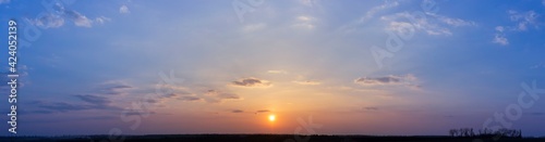 Panorama of blue and orange sunset, sky with clouds, evening over the field. Silhouettes of trees in the valley