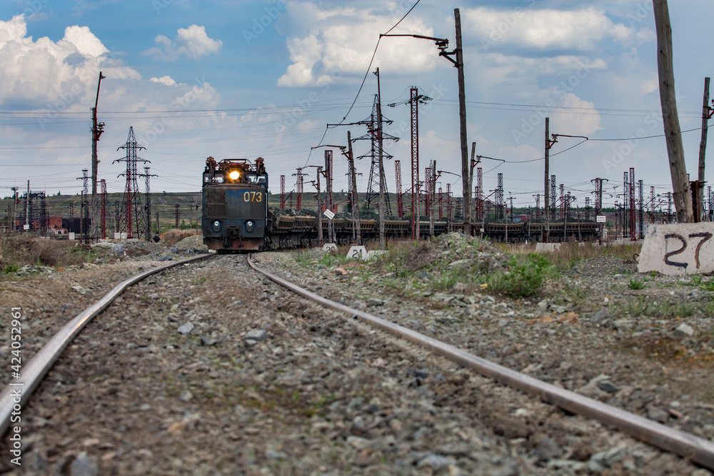 Rudny/Kazakhstan - May 14 2012:  Open-pit mining iron ore. Railway  train and diesel locomotive with light on rails in quarry. blue sky with clouds.