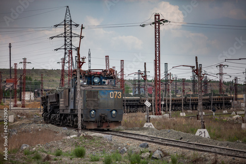 Rudny/Kazakhstan - May 14 2012: Open-pit mining iron ore. Railway train and diesel locomotive on rails in quarry. Blue sky with clouds. 