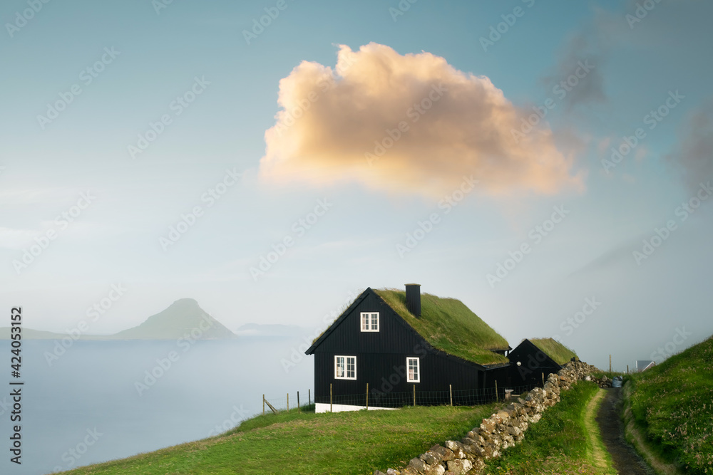 Obraz premium Foggy morning view of a house with typical turf-top grass roof and beauty sunset cloud in the Velbastadur village on Streymoy island, Faroe islands, Denmark. Landscape panorama