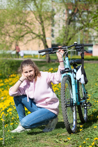 Caucasian teenage girl wearing pink hoody sitting on grass and holding her blue bike