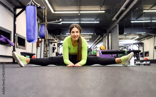 Young woman performs splits and stretching exercises on a workout in the gym