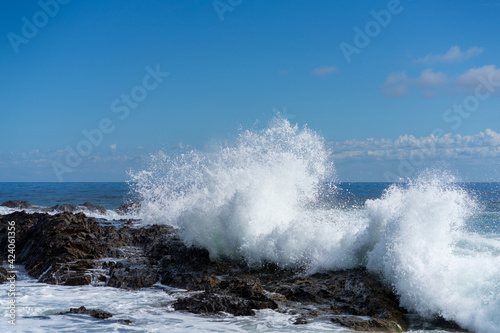 Waves crashing over black rocks in frozen motion on a warm sunny summer day. Blue and white sea colors. Rainbow Bay, Gold Coast, Queensland, Australia.