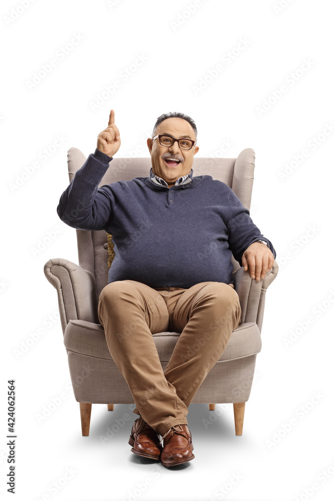 Cheerful mature man sitting in an armchair and pointing up