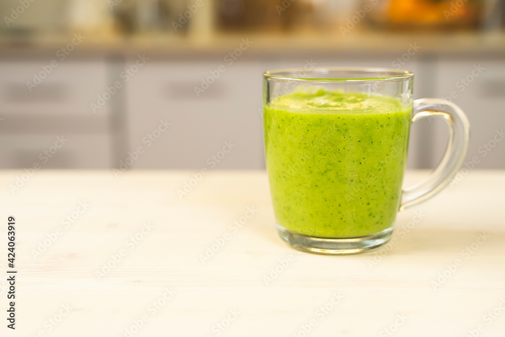 Glass cup with green spinach and kale health smoothies with straw in kitchen table Glass cup with green spinach and kale health smoothies with straw in kitchen table