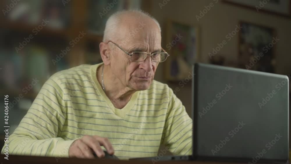Aged concentrated man in glasses looking to laptop screen and studying online. Aged concentrated man in glasses looking to laptop screen and studying online.