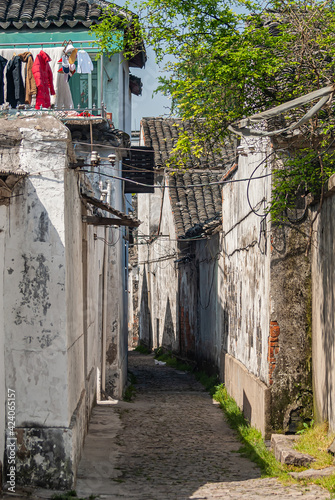 Tongli, China - May 2, 2010: Narrow alley between white platered house walls with green foliage above and colorful laundry on top of one house. photo