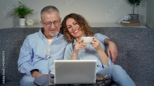 A happy middle-aged couple watches a funny movie on their laptop and laughs.
