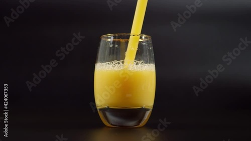 Drinking orange juice from straw. Close up on luxury glass filled with orange juice standing on dark background. photo