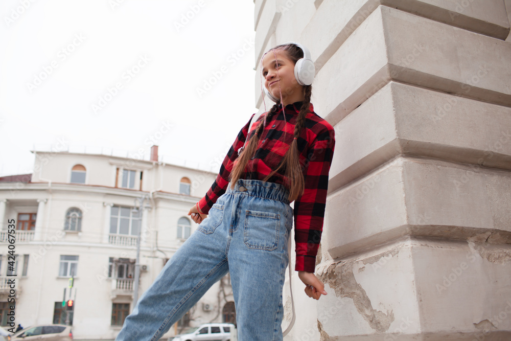 preteein girl in white headphones listen musik, walking outdoor in the street