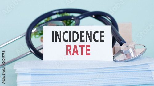 Card with words incidence rate, stethoscope, face masks and flower on table
