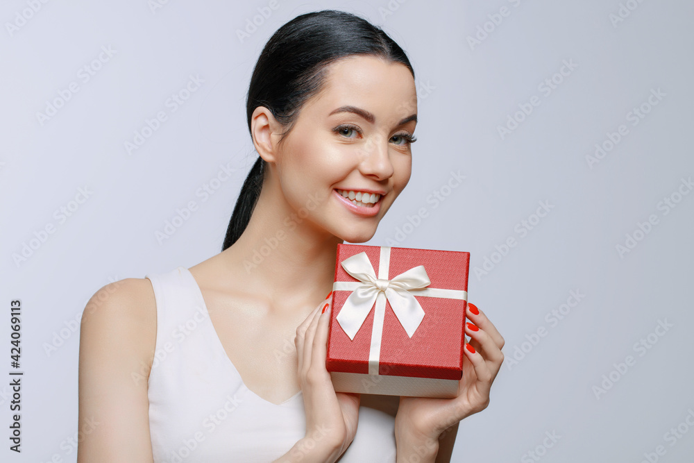 Cheerful woman holding present box in studio on gray background. Smiling beautiful young girl expressing happy emotions. Seasonal discounts and sale. Cheerful woman holding present box in studio on gray background. Smiling beautiful young girl expressing happy emotions. Seasonal discounts and sale.