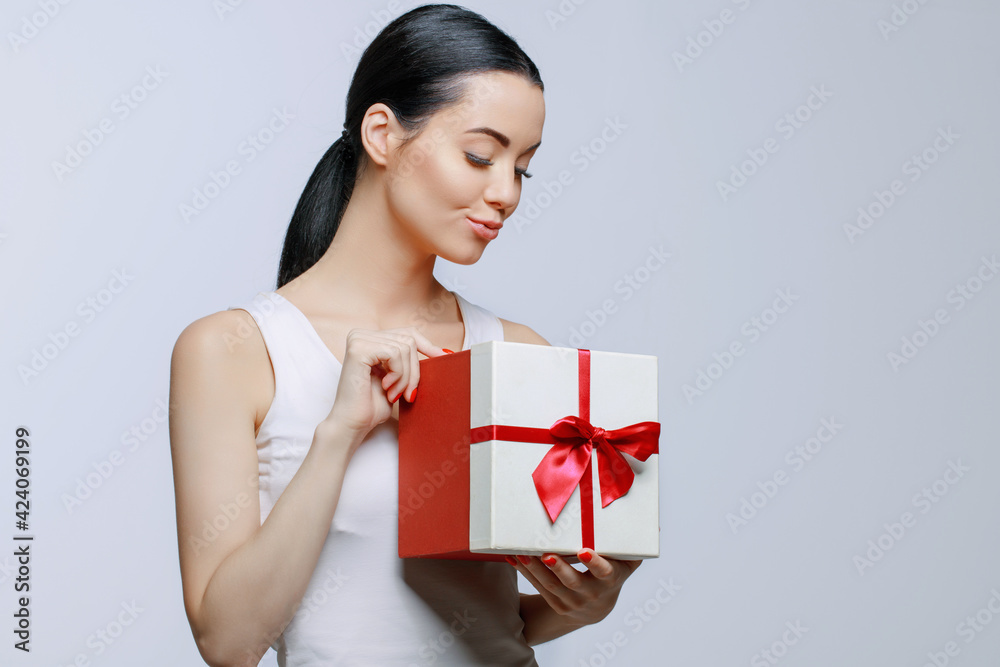 Cheerful woman holding present box in studio on gray background. Smiling beautiful young girl expressing happy emotions. Seasonal discounts and sale. Cheerful woman holding present box in studio on gray background. Smiling beautiful young girl expressing happy emotions. Seasonal discounts and sale.