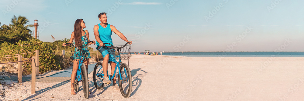 © Maridav - Florida beach vacation couple biking sport rental bikes recreational activity happy watching sunset on Sanibel Island by the Lighthouse. Young woman and man riding bicycles. Summer people lifestyle.