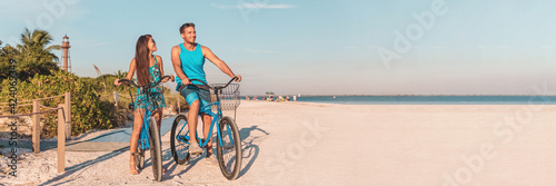 Florida beach vacation couple biking sport rental bikes recreational activity happy watching sunset on Sanibel Island by the Lighthouse. Young woman and man riding bicycles. Summer people lifestyle.
