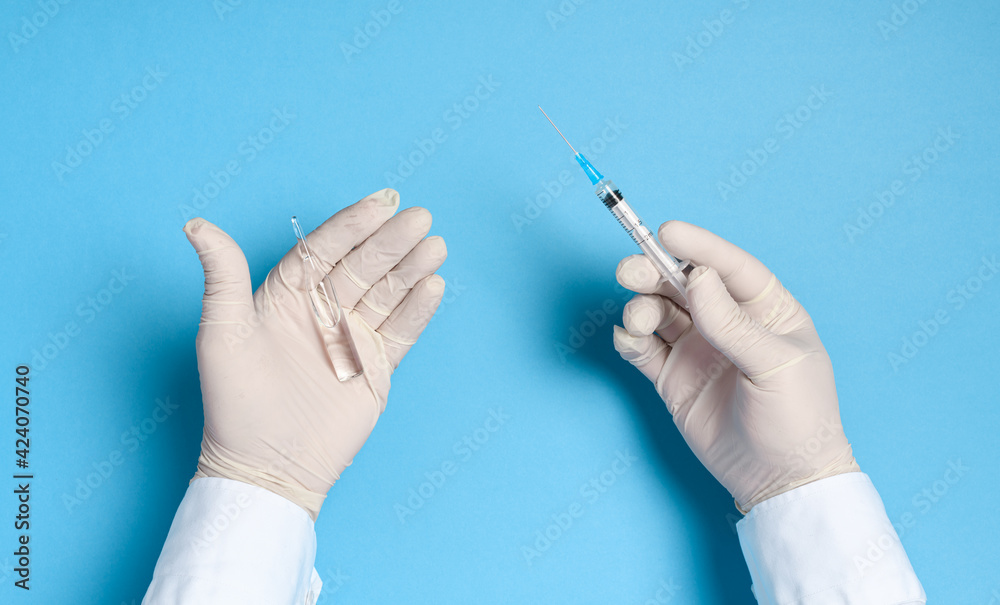hands in medical gloves with a syringe on a blue background, imitation of a coronavirus vaccine, prevention of infection with viruses and bacteria hands in medical gloves with a syringe on a blue background, imitation of a coronavirus vaccine, prevention of infection with viruses and bacteria