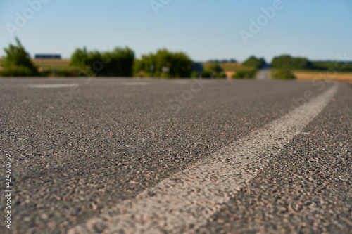 soft focus asphalt road surface with white markings close-up from the low shot. blured country road and field with forest in summer. High quality photo. Travel, tehnology, nature comcept.