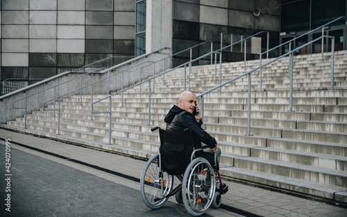 Disabled man on wheelchair stopped in front of stairs and talking on the phone. © Daniel Jędzura