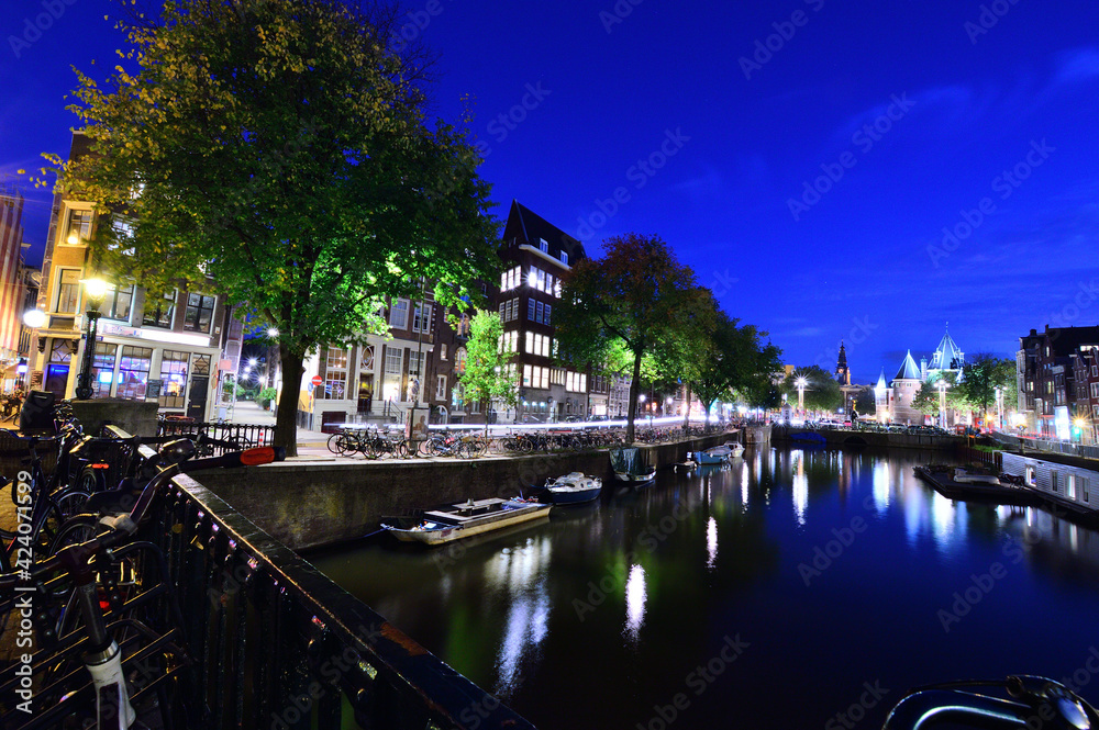 Bicycles on the canal in Amsterdam, Netherlands at night illuminated by colorful lights.