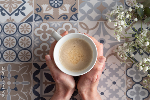 Manos sujetando café caliente sobre mantel de mosaico