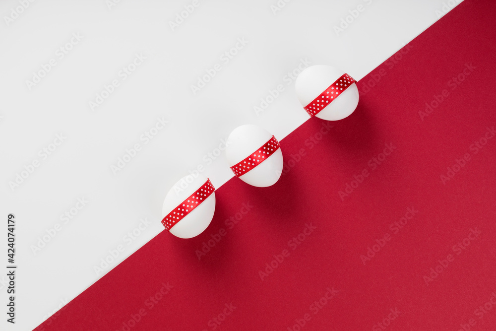 Easter Concept. White Easter eggs decorated with red ribbon on red and white paper background. Copy space. Flat lay. Easter Concept. White Easter eggs decorated with red ribbon on red and white paper background. Copy space. Flat lay.