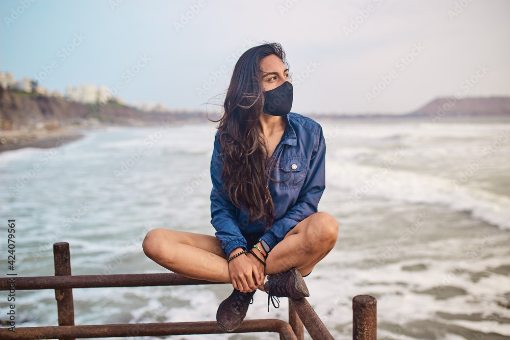 mujer joven con mascarilla feliz en la playa. Momento de relajacion a orillas del mar durante un atardecer. Fondo de olas y mar mujer joven con mascarilla feliz en la playa. Momento de relajacion a orillas del mar durante un atardecer. Fondo de olas y mar