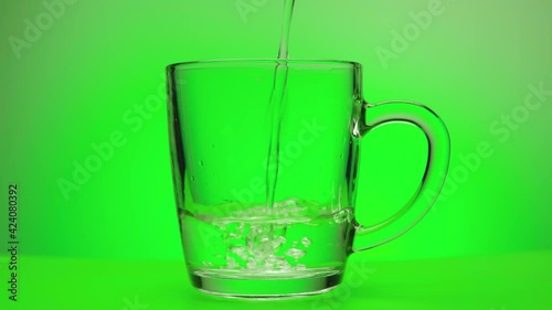Water is poured into a transparent glass on a green background. Close-up.