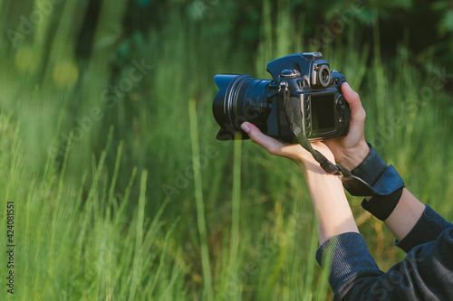 Close-up, professional photo-video camera in the hands of a girl. Against the background of green nature and forest.