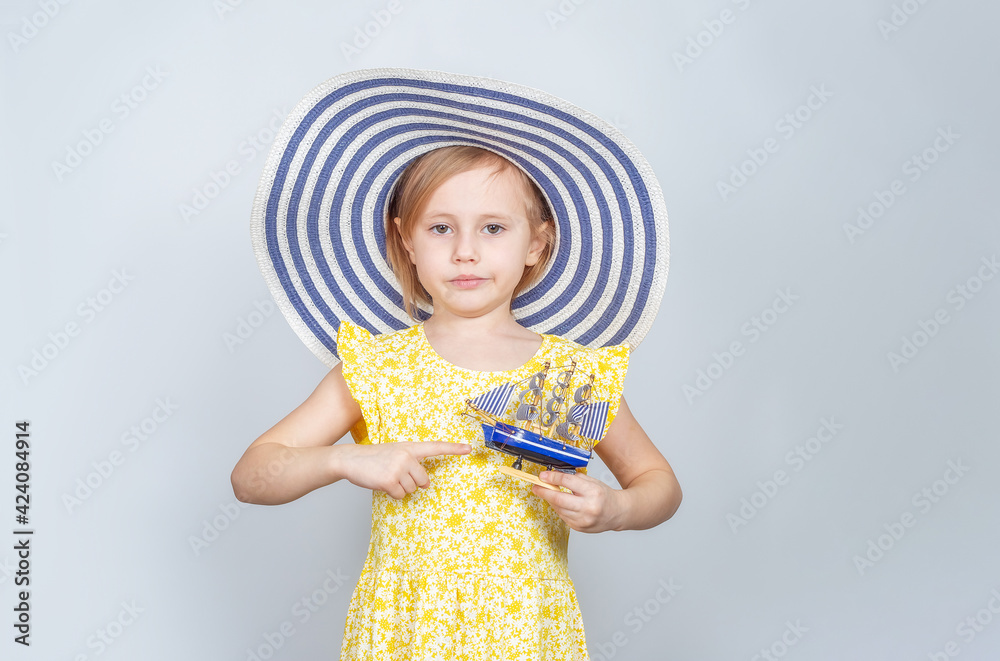 A girl in a wide-brimmed hat holds a toy boat in her hands.