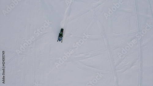 Aerial top view of a man riding a snow covered field on a snowmobile. Clip. Concept of winter sport and active lifestyle. photo