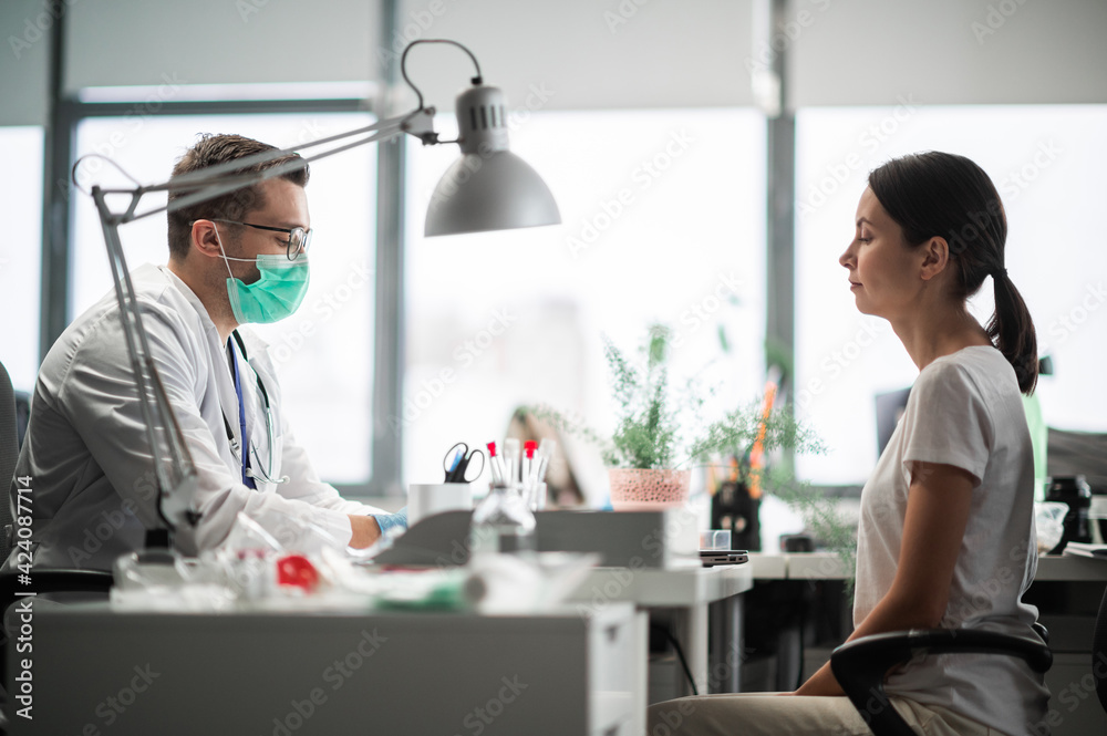 A young doctor is receiving a female patient at a desk in his office