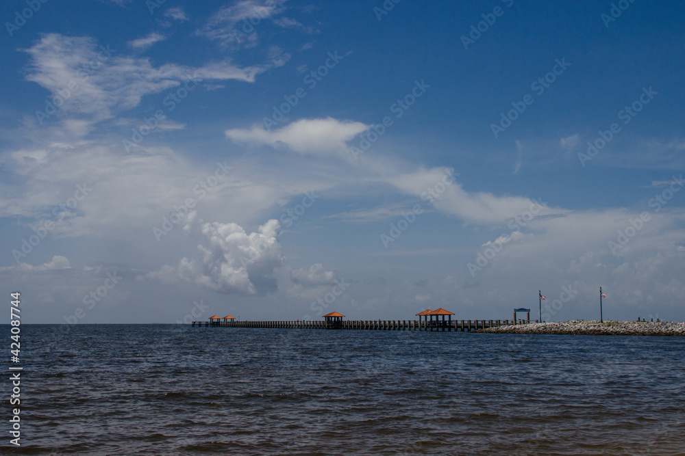 Seascape. A pier in the ocean on the sides of which American flags hang on poles on a summer sunny day. Ken Combs Pier, Gulfport, Massachusetts, USA - 7-4-2019