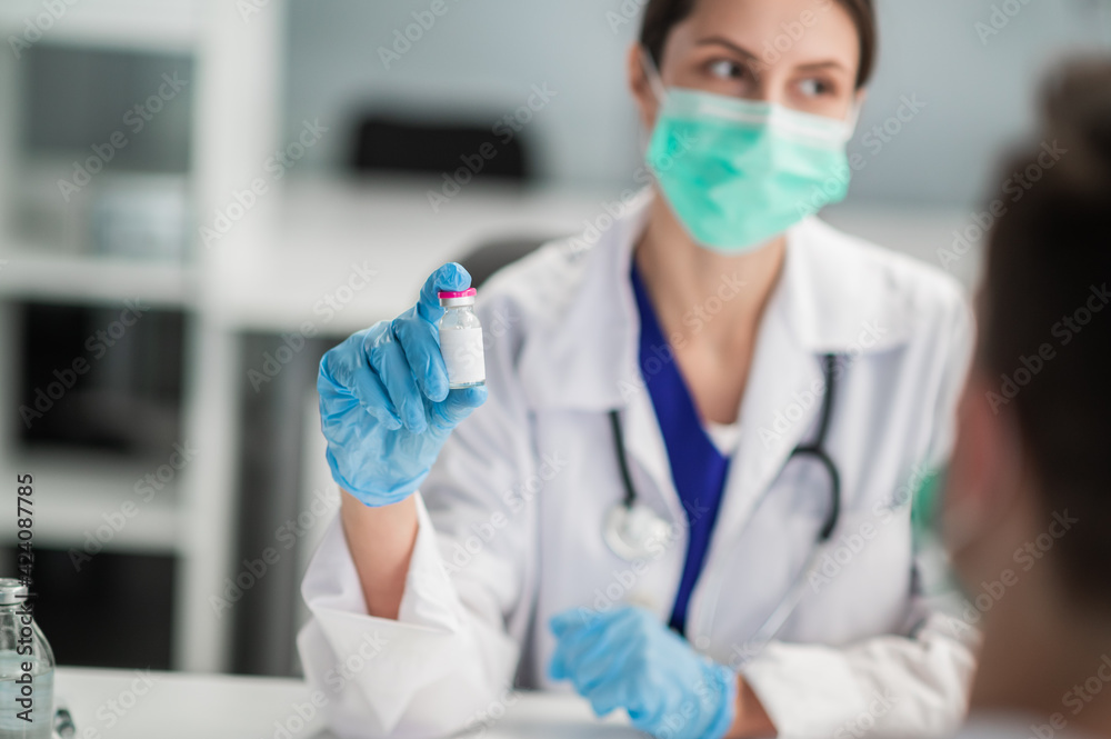 A young medical woman holds a bottle of vaccine in her hands and shows it A young medical woman holds a bottle of vaccine in her hands and shows it