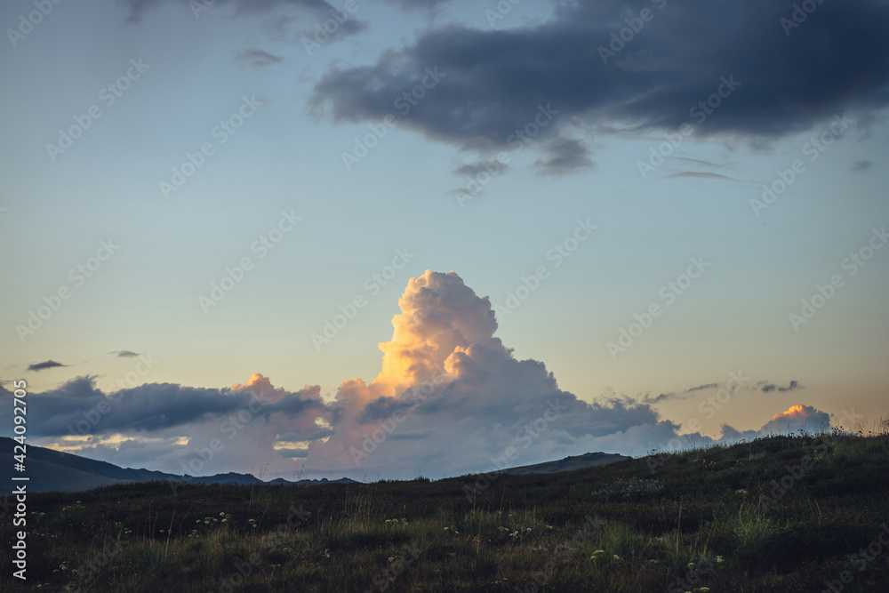 Impressive mountain scenery with orange big cloud in form of explosion in sunset. Sunrise landscape with beautiful huge cloud of illuminating color. Scenic view to yellow giant cloud in dawn sky.