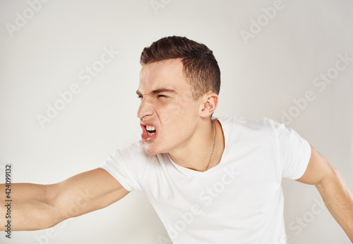 Emotional man in a white T-shirt gestures with his hands on a light background model stress irritability