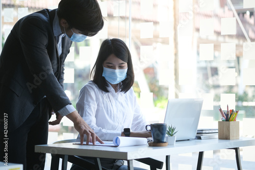 Two young business people wearing protective mask working together in office.