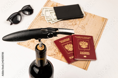 the neck of a bottle of red wine with a corkscrew in the cork, a map of the world, two passports, money in a black wallet and sunglasses. selective focus. inscription - passport Russian Federation