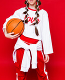 Basketball ball in the hands of a girl dressed in sportswear. Studio shot on red background
