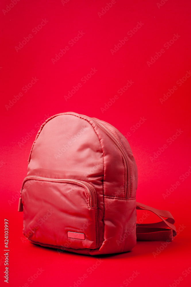 Naklejka premium Children's backpack in pink fabric with shoulder straps, shot against a rich red background.