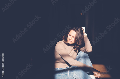 Beautiful young serious woman sitting on the floor in spot of light, fashion portrait with harsh shadows.