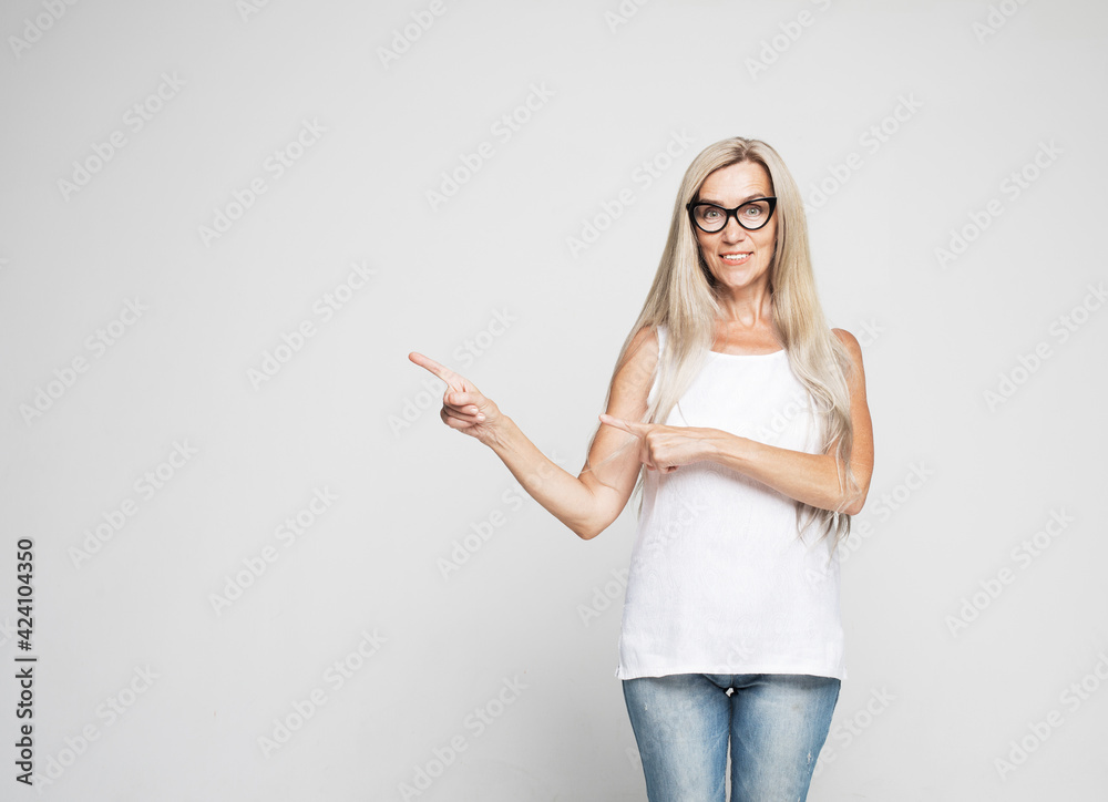 Smiling senior gray-haired woman isolated on gray studio background pointing with finger at blank copy space aside, happy positive aged female show at vacant advertising spot Smiling senior gray-haired woman isolated on gray studio background pointing with finger at blank copy space aside, happy positive aged female show at vacant advertising spot
