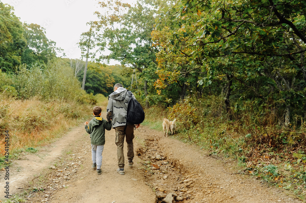 dad and son in military khaki clothes go off-road with a backpack for traveling. family hiking trips. local tourism. travel with pets. selective focus dad and son in military khaki clothes go off-road with a backpack for traveling. family hiking trips. local tourism. travel with pets. selective focus