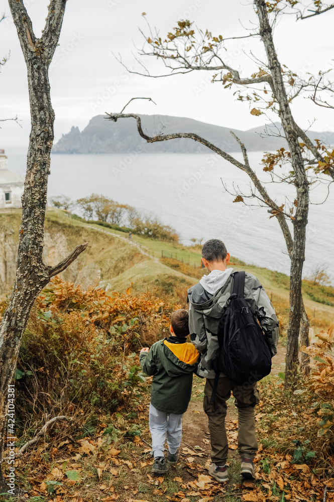 Naklejka premium father and son in military khaki clothes travel through the mountains with backpack. family hiking trips. local tourism small group. vertical travel content. selective focus