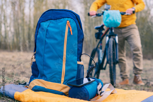 Portable charger power bank charges a smartphone in nature with backpacks in the background of a cyclist with a bicycle. Time to travel.