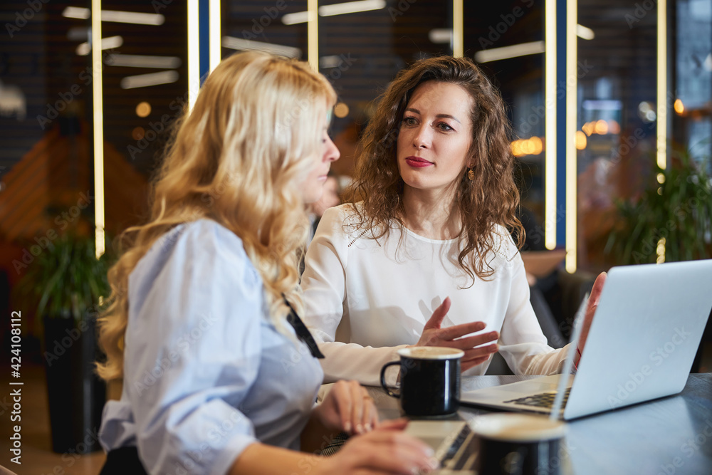 Charming young women discussing business project at work Charming young women discussing business project at work